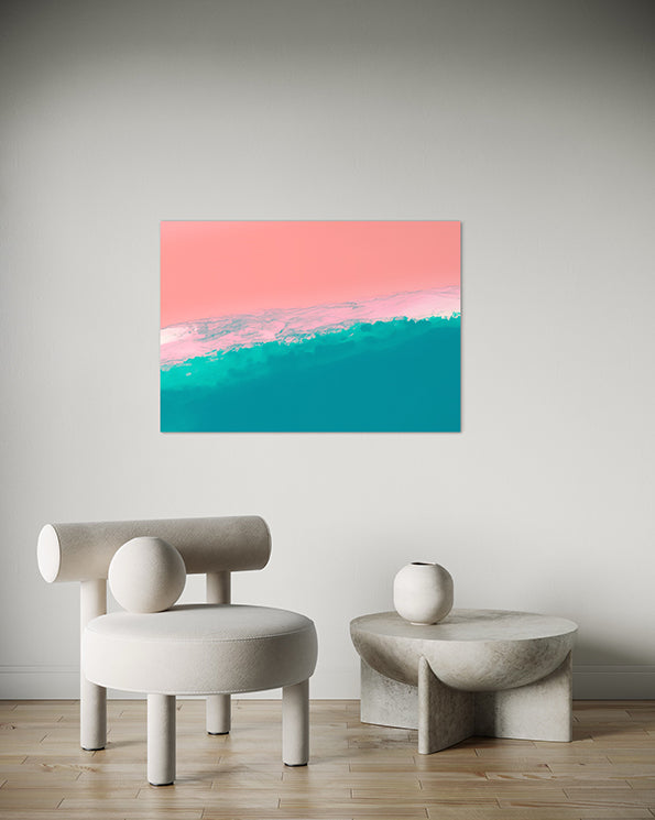 abstract artwork featuring ocean shoreline from above, pink sand meets the white wash in the middle of the frame with blue ocean waves, wall art hanging in living room above armchair and low lying white coffee table.