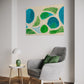 abstract artwork depicting aerial view of a beach with sand and grass shrubs and pools of water with shaky brush strokes making it seem wind swept. Abstract wall art hanging in living room above a grey armchair