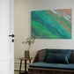 tidal whispers unique wall art print, waves gentle lapping at the shore in green and aqua tones. wall art in living room above a blue green coastal lounge.
